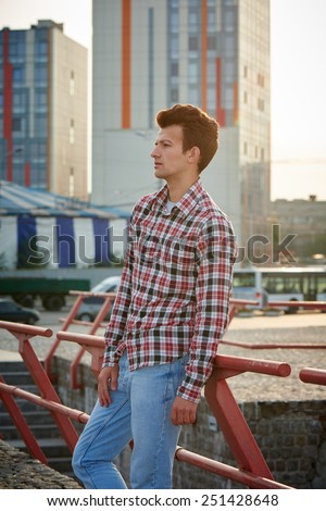 Handsome man, fashion model, with toupee standing outdoors in summertime over city background