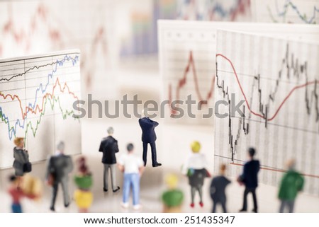 Banker stands on a pedestal of coins and looks at boards with different charts. Royalty-Free Stock Photo #251435347