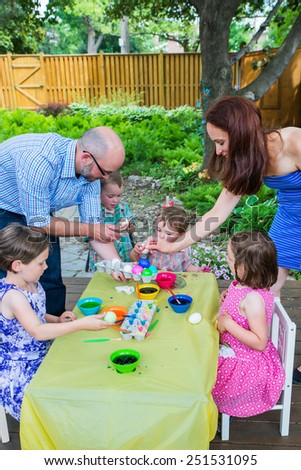 Family with children painting and decorating eggs together during the spring season in a outdoor garden setting.  Mother and father help the kids color dye their Easter eggs.  Part of a series.  