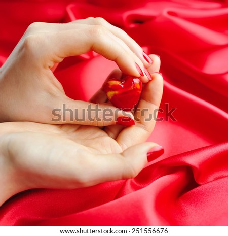 Decorative Heart in women's hands against a background of red silk