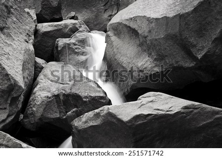 A black and white photograph of water streaming down rocks at Yosemite Falls in Yosemite National Park.