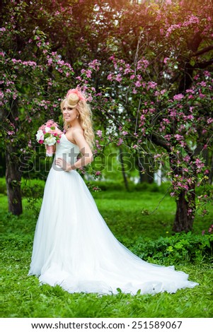 Very beautiful happy bride blonde curly hair in a white dress and delicate unusual bouquet in hand, against the background of Apple blossoms in full growth