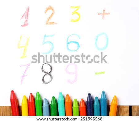 Crayons lying on a paper with children's drawing digit, number, sign. Selective focus, copy space background