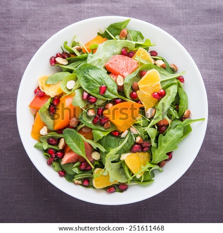 Fresh salad with fruits and greens on dark canvas background top view. Healthy food.