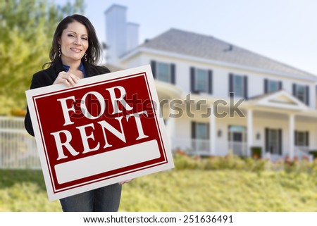 Smiling Hispanic Female Holding For Rent Sign In Front of Beautiful House.