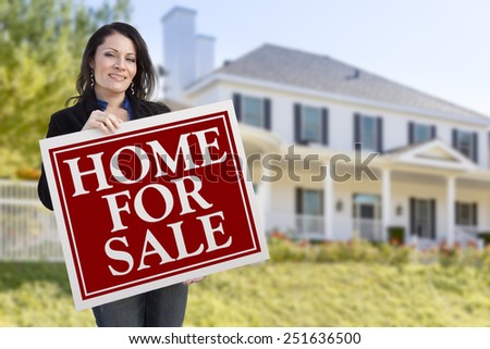 Smiling Hispanic Female Holding Sold For Sale Sign In Front of Beautiful House.