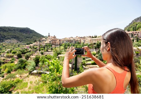 Tourist taking picture of Deia Village in Mallorca. Travel woman hiker using smartphone app to take a landscape photo of the Unesco World Heritage site on Majorca, Balearic Islands, Spain.