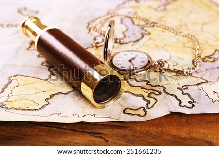 Spyglass, pocket watch and world map on wooden table background