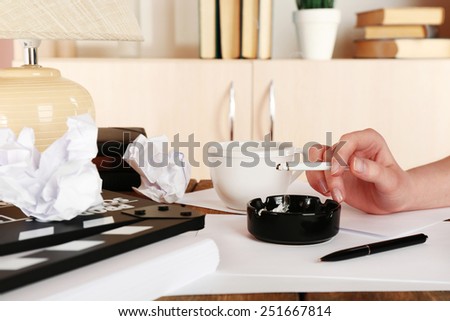 Female hand with cigarette at desktop with moving clapper and working mess on light cupboard background