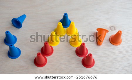 Multiple colour mini plastic safety cones on wooden surface. Slightly de-focused and close-up. Shot with natural light. Concept of work in progress. Copy space.