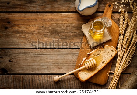 Honey in a jar, slice of bread, wheat and milk on an old vintage planked wood table from above. Rural or rustic style breakfast concept. Background layout with free text space. Royalty-Free Stock Photo #251766751