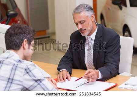 Salesman showing client where to sign the deal at new car showroom