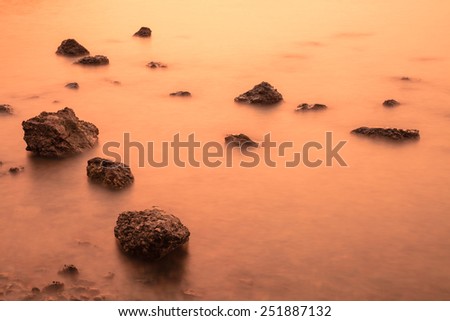Long exposure of rocks in golden sea before sunset