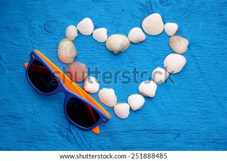 valentines day picture. sunglasses and shells on shape of heart on wooden blue background with place for text