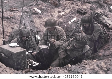 U.S. soldiers of a shore fire control group operating Signal Corps radios. One man cranks the hand generator, while another uses a hand-held radio set. June 6-8, 1944, Normandy, France. Royalty-Free Stock Photo #251930041