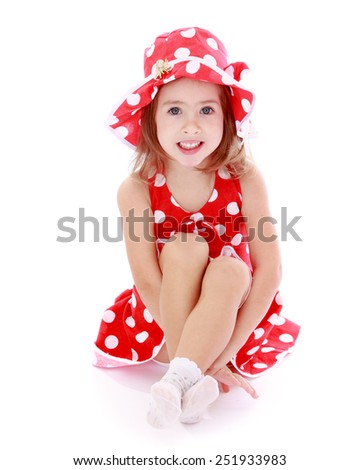 beautiful little girl in a red polka-dot dress sitting on the floor.Isolated on white background, Lotus Children's Center.
