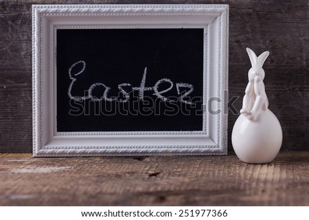 Symbol of Easter rabbit and board with word Easter on wooden background. Selective focus.