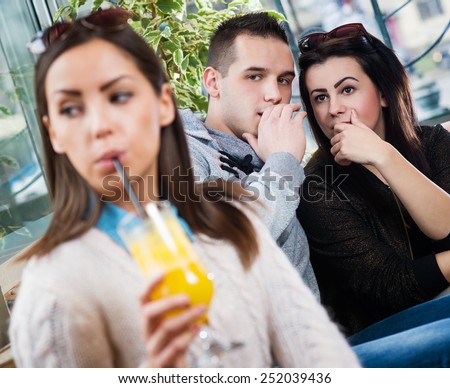 Young beautiful female sitting in cafe out of focus, while the two gossiping behind.