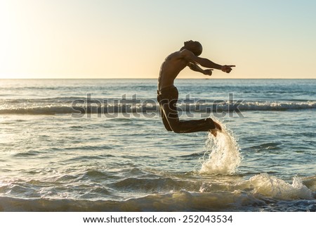 Healthy, fit and muscular black african american man jumping for joy on a beach during sunset while on vacation. Concept of a happiness, life and wellness Royalty-Free Stock Photo #252043534