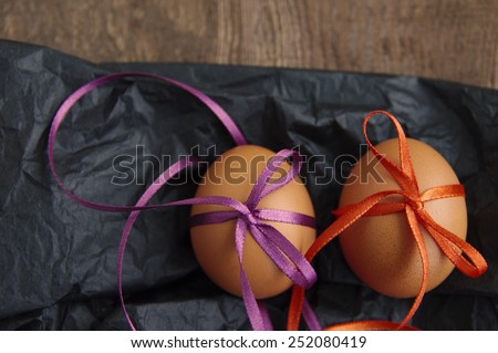 two Easter eggs with bright color tapes on black crumpled paper on a brown wooden background