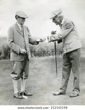 A splendid long putt deserves a dime'. John D. Rockefeller hands Harvey Firestone a dime during a golf match at Orvond Beach, Florida. Jan. 31, 1930. Royalty-Free Stock Photo #252142198