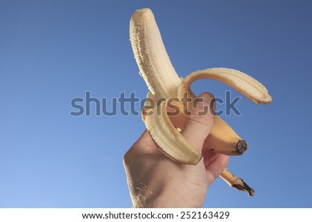 A hand holding banana outside with sky view