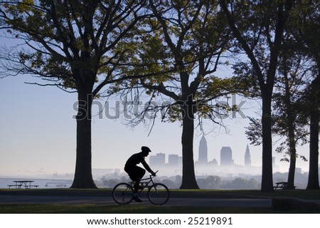 Silhouette of biker riding in park with trees and Cleveland skyline in background on a foggy morning.