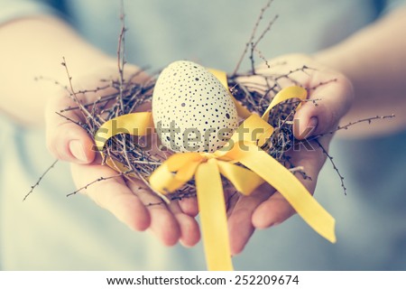 Hands holding modern painted easter egg in a small nest. Toned picture