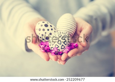 Hands holding modern painted easter eggs and violet flowers. Toned picture