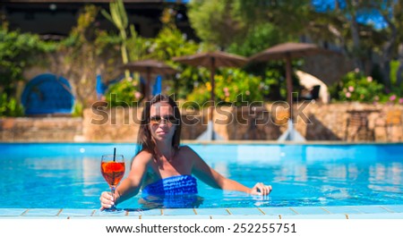 Beautiful young woman in swimming pool with cocktail