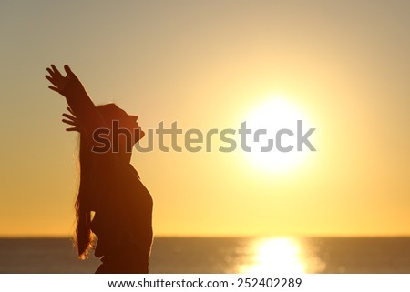 Woman breathing fresh air at sunset on the beach and raising arms