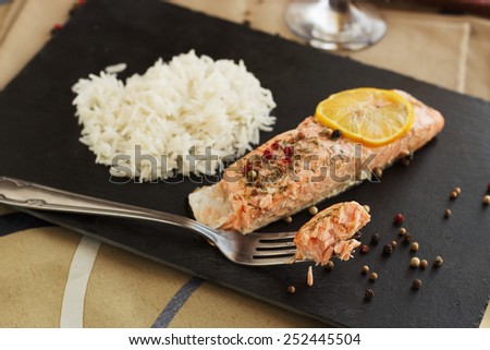 Fresh salmon steamed with olive oil, lemon juise, dill and pepper served on black plate with steamed rise and white vine.