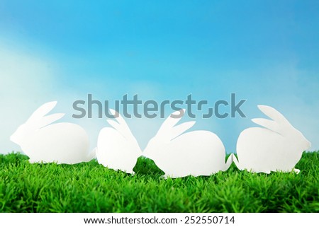 Paper Easter rabbits on green grass, on sky background
