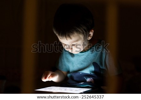 kid with tablet in the dark laying in bed and reading