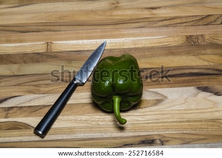 Green Bell pepper and paring knife on a teak cutting board