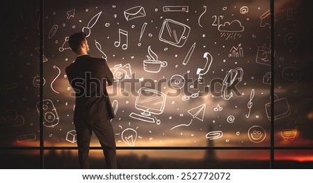 Businessman drawing media icons on glass window, bokeh cityscape background 