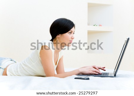 Photo of teenage girl lying on bed and pressing laptop keys at home