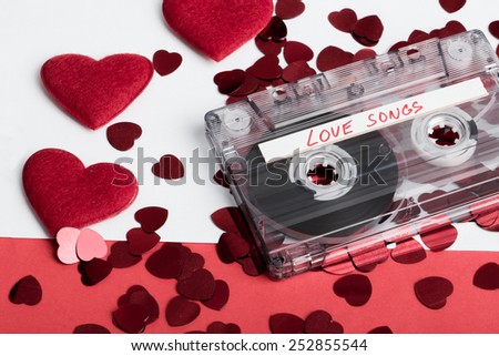 Audio cassette tape on red backgound with fabric heart, Valentine postcard. Love concept with evelope and confetti