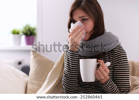 Sick woman covered with blanket holding cup of tea sitting on sofa couch Royalty-Free Stock Photo #252860461