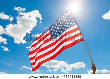 American flag waving in blue sky with sun behind it