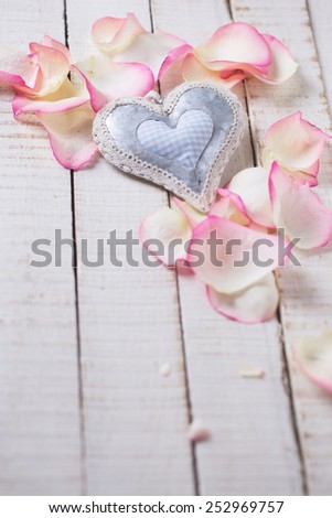 Decorative heart on rose petals on white wooden background. Selective focus.