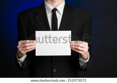 Business and advertising topic: Man in black suit holding a white blank card in his hand on a dark blue background in studio isolated