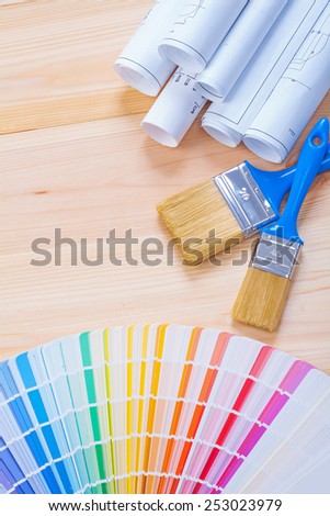 color palette with paintbrushes and rolled white blueprints on wooden background 