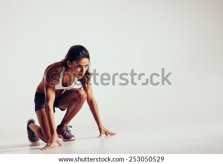 Female athlete in position ready to run over grey background. Determined young woman ready for a sprint. Royalty-Free Stock Photo #253050529