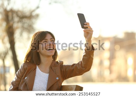Woman taking selfie photo with a smarphone in winter sitting in a bench in a park