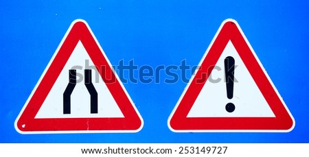 narrow road and exclamation mark signs on blue background