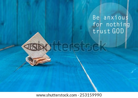 Inspirational motivating quote saying that God has everything in control. Christian fish symbol carved in wood and blue vintage wooden background