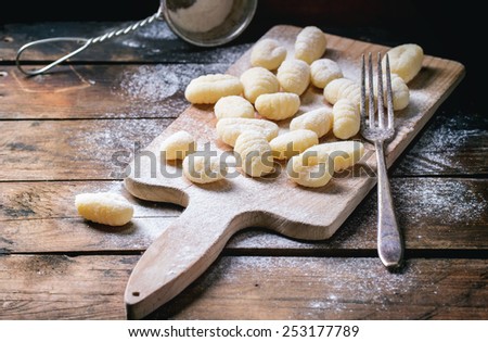 Uncooked homemade potato gnocchi with fork and strainer on vintage cutting board over wooden table with flour. See series. Royalty-Free Stock Photo #253177789