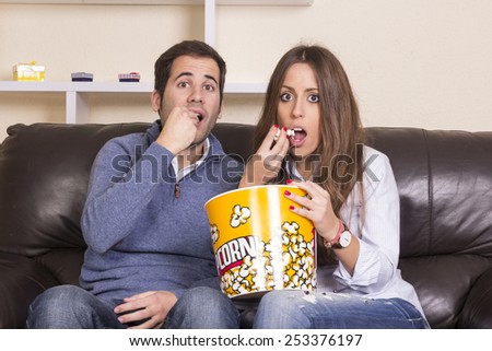 Couple watching film on sofa eating popcorn Royalty-Free Stock Photo #253376197