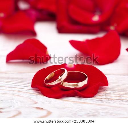 Invitation Wedding rings and red roses on wooden desk, square. Selective focus, the background is blurred